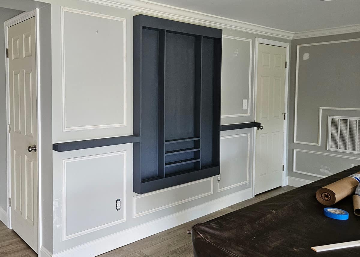 A basement room with a custom pool cue rack on the wall, shelves, and picture frame molding.