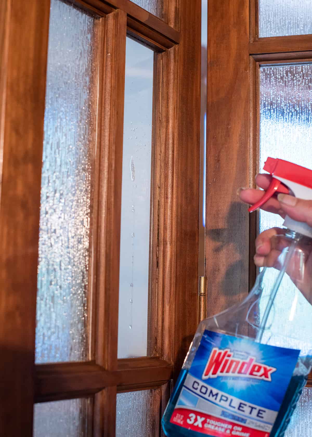A hand spraying Windex glass cleaner on a window.
