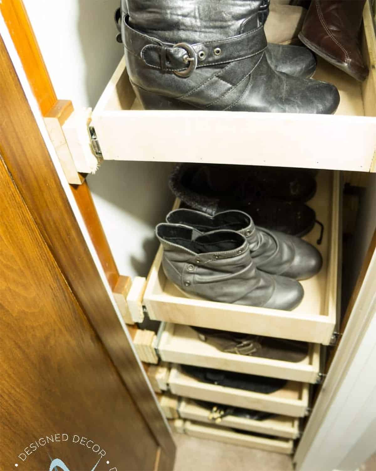 Shoes on pull out shelves in a small closet.