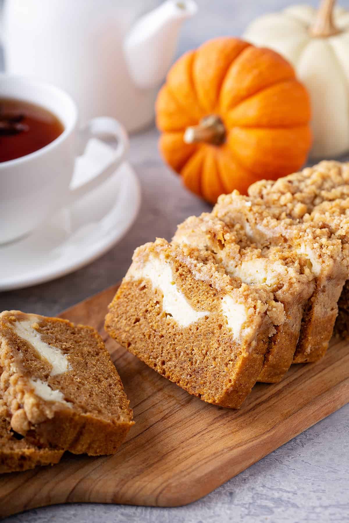 Sliced Pumpkin Cream Cheese Bread on a wood platter with mini pumpkins in the background.