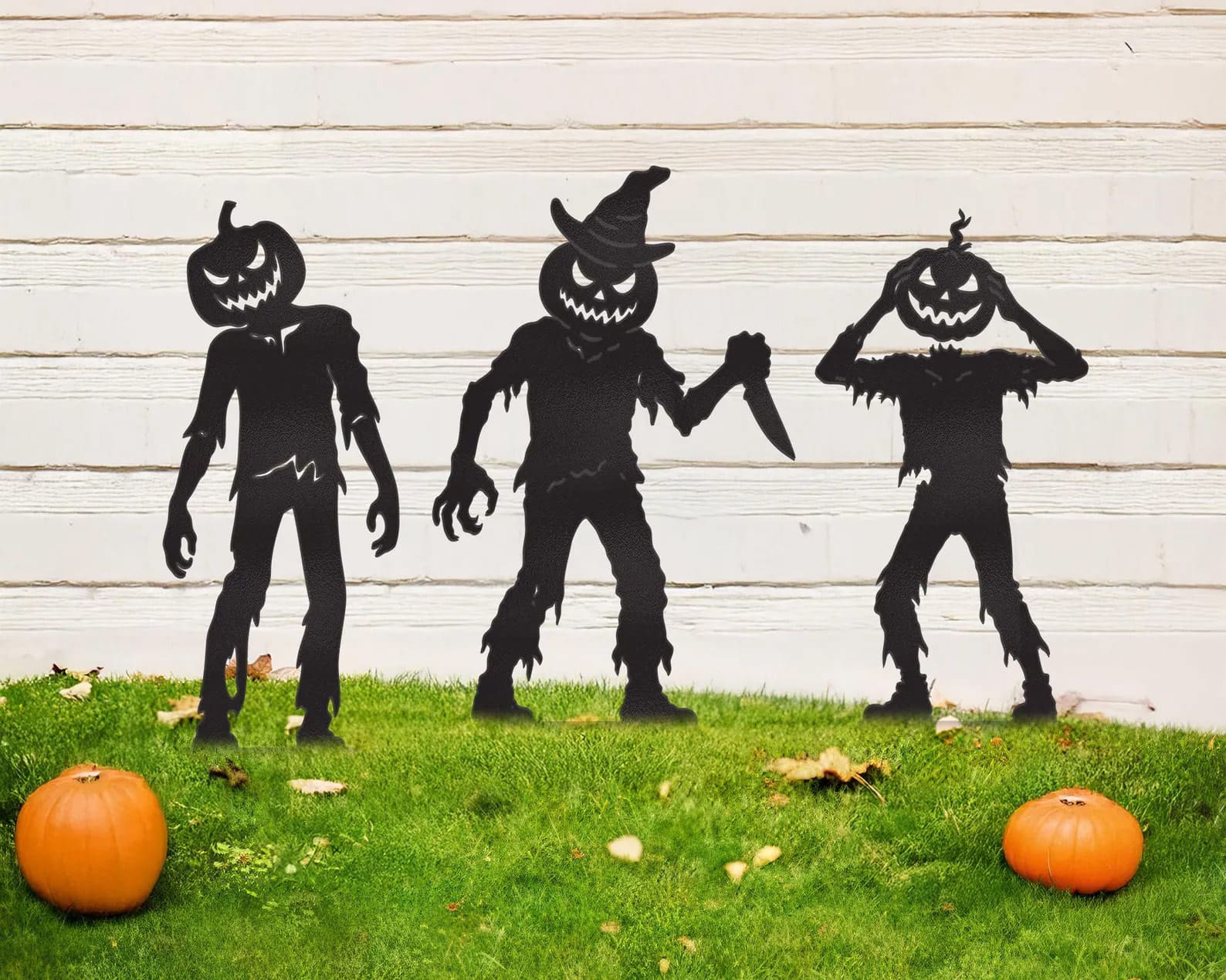 Three pumpkin headed demon figures in black on top of grass for Halloween.