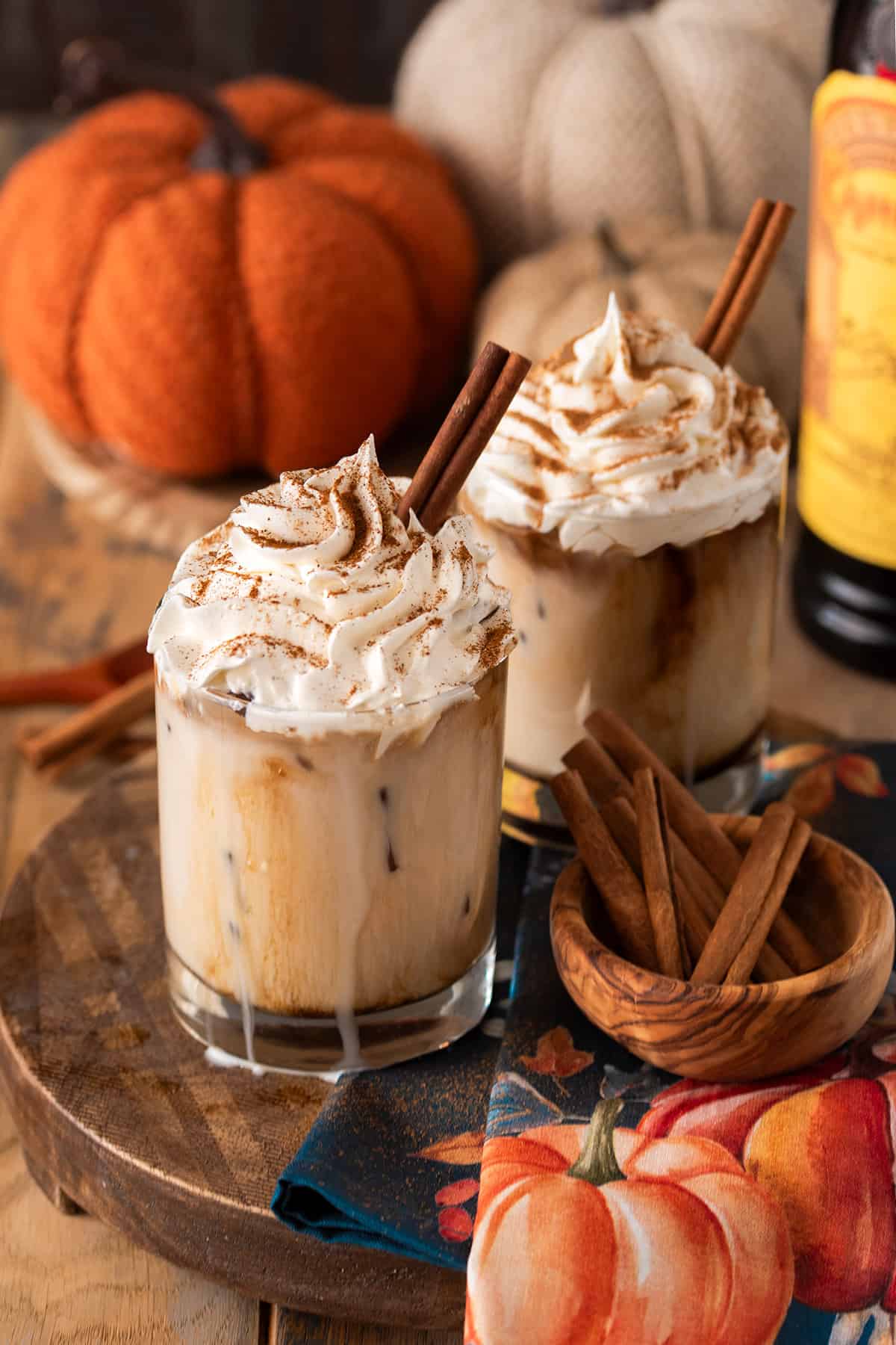 Pumpkin White Russian cocktails with pumpkin spice sprinkled on top and cinnamon sticks to the side.