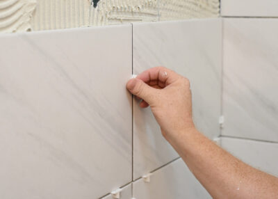 Man laying a tile spacer in between two large tiles.