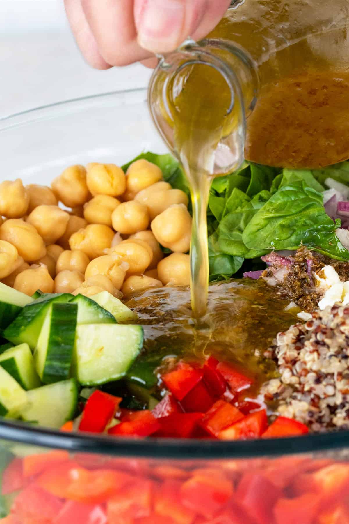 Vinaigrette dressing being poured over Mediterranean chickpea and quinoa salad in a bowl.