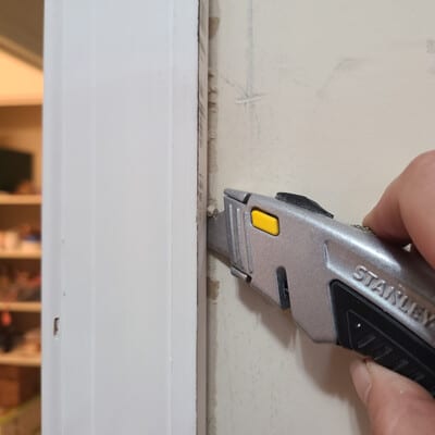 Razor knife cutting caulk around door casing.