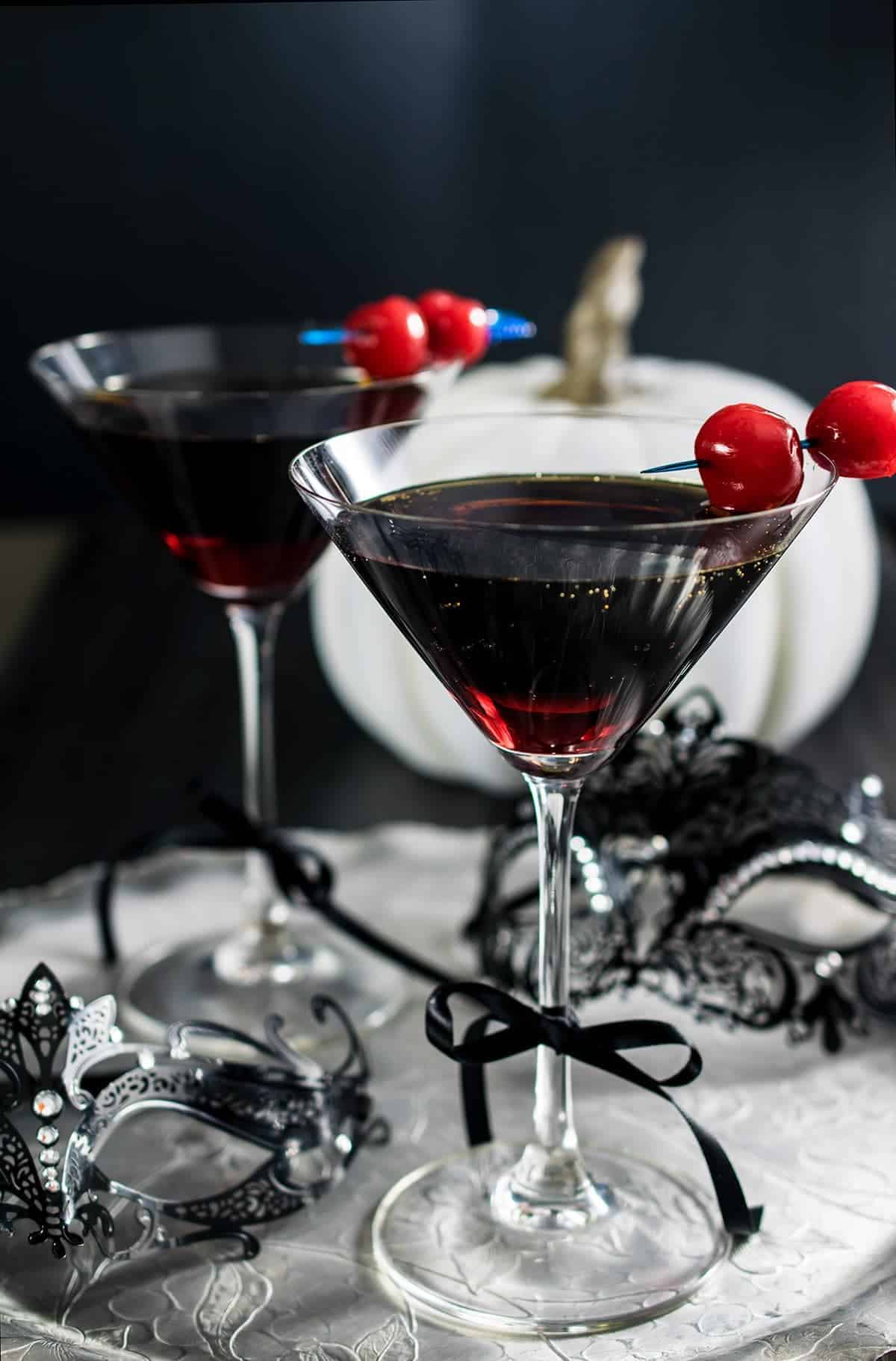 Halloween red martini cocktail with cherry garnish on masquerade themed tray. 
