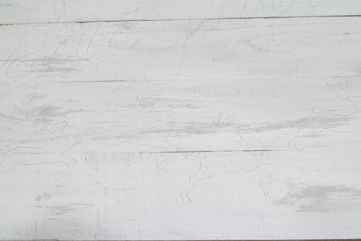 Detail of DIY pallet sign with chalky white distressed finish and outline of Santa's sled stencil.