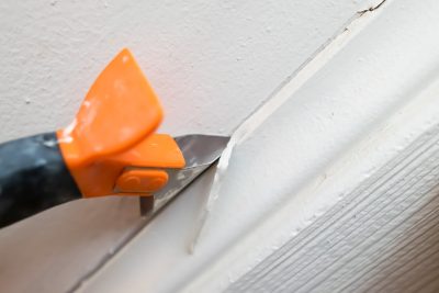 A caulk scraper removing the caulk on a baseboard.