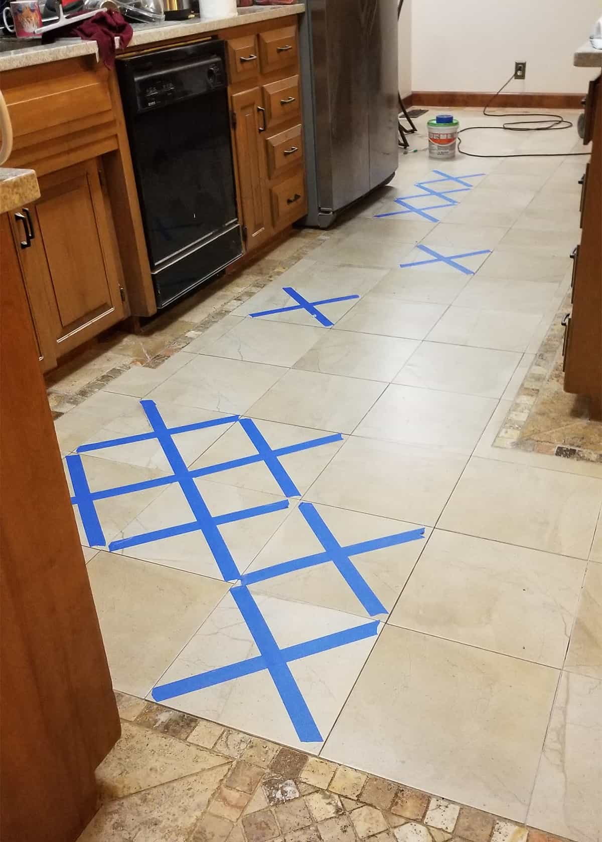 Kitchen floor marked with painter's tape to show which tiles were replaced and still drying.