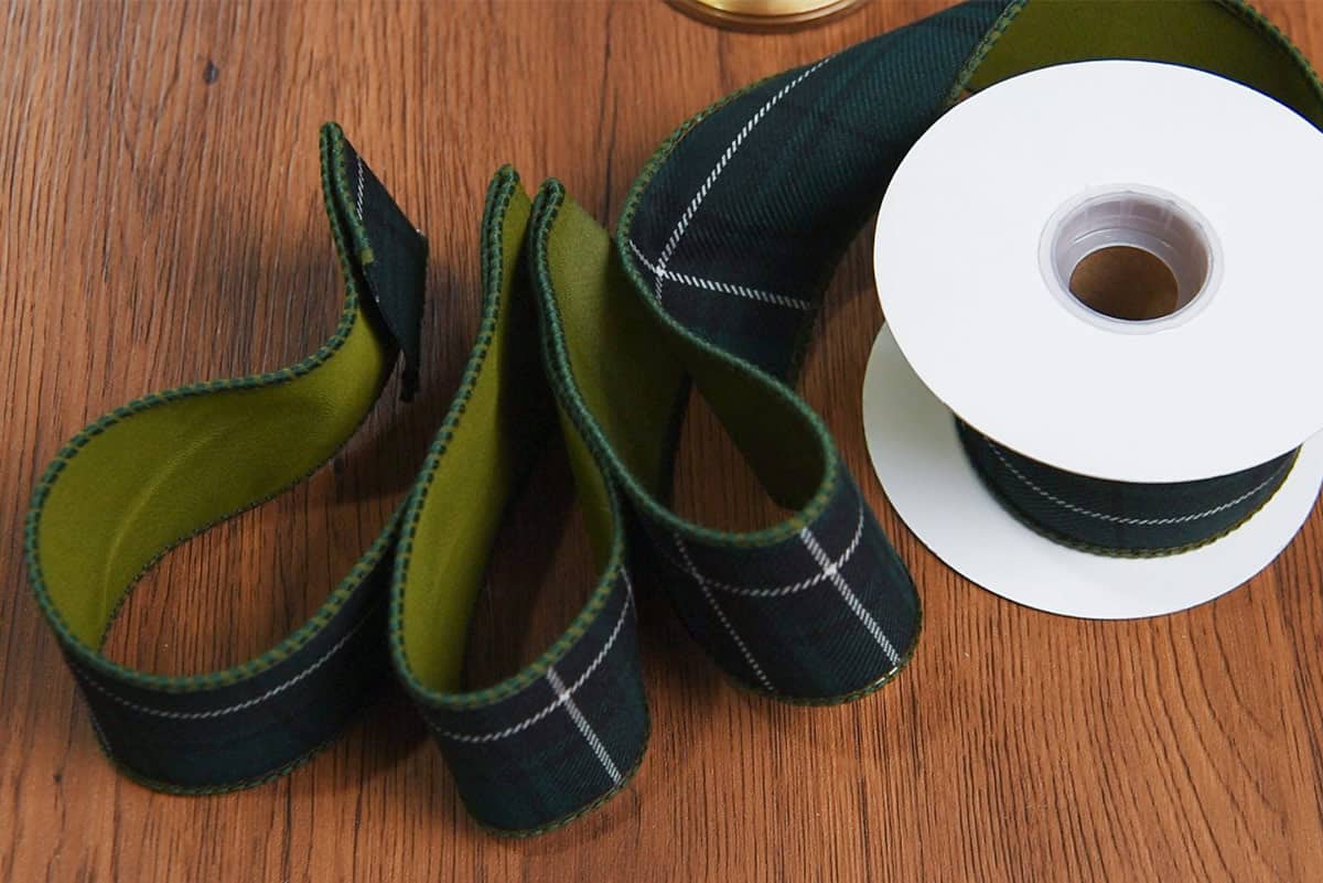 A spool of green tartan ribbon formed into loops on a desk.