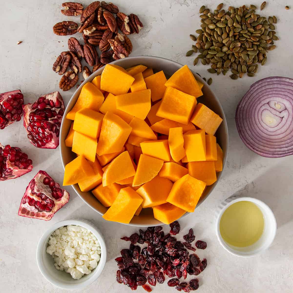 Salad topping ideas including red onion, pepitas, cranberries, goat cheese, pecans, and pomegranate flat lay on a table.