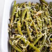 Oven roasted green beans sprinkled with parmesan and garlic in a casserole dish.