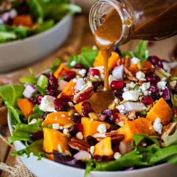 A bottle of balsamic vinaigrette being poured over a salad of squash and winter fruits.