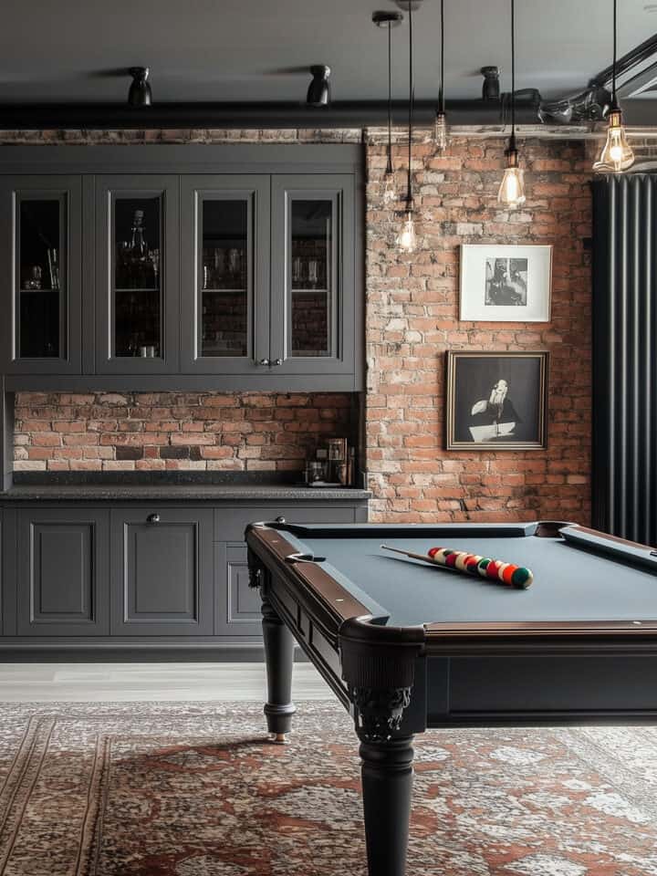 A basement bar area with brick wall, charcoal gray cabinets, and pool table in a moody color palette.