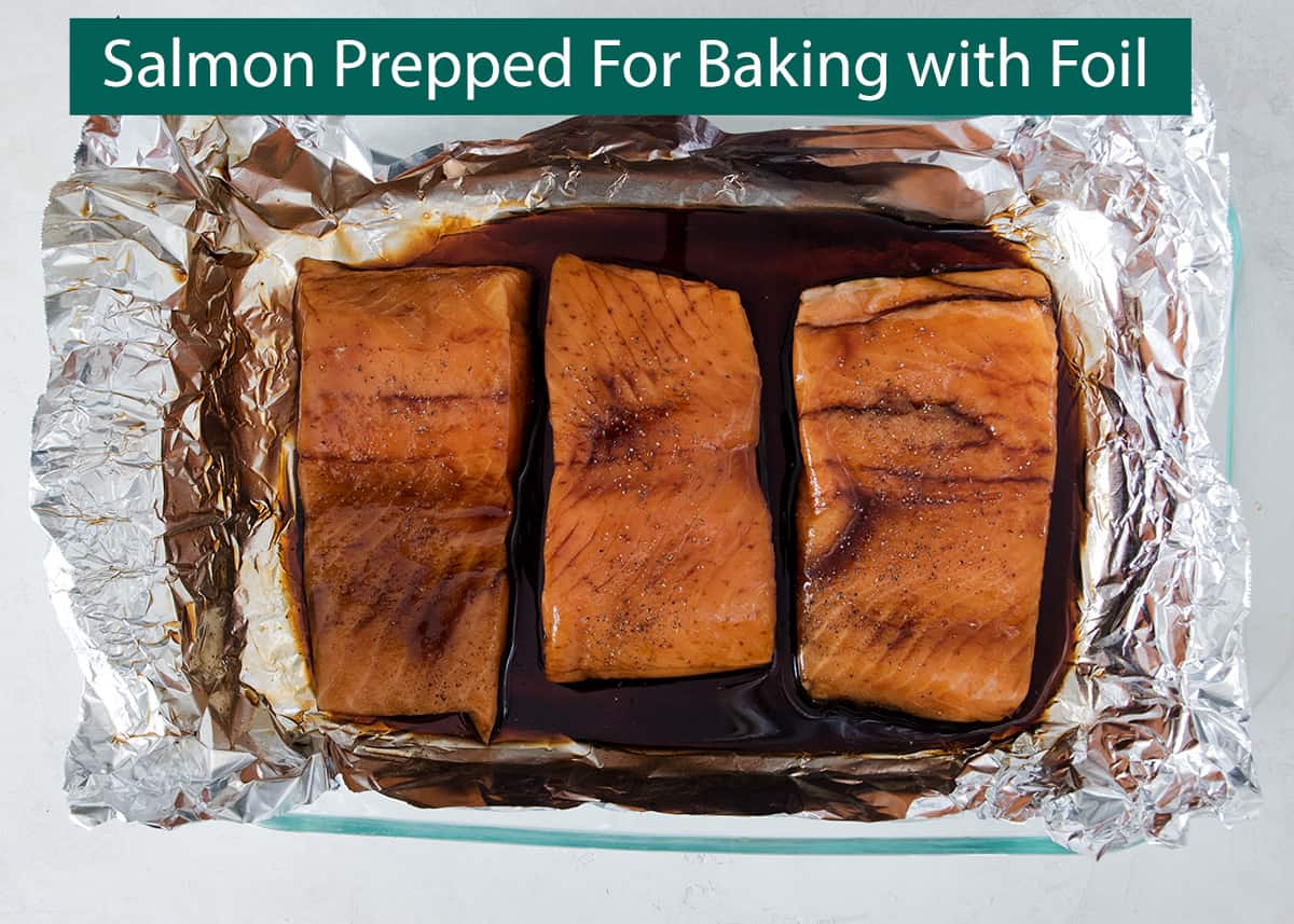 Salmon filets in foil lined pan ready for baking with teriyaki sauce poured over.
