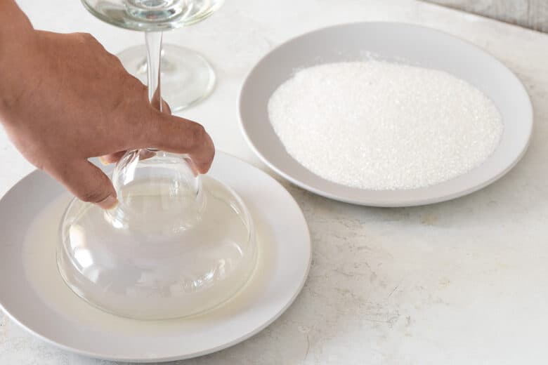 Demonstration of salt rimming a cocktail glass. A glass is dipped into a plate filled with lime juice while another plate is filled with kosher sea salt.