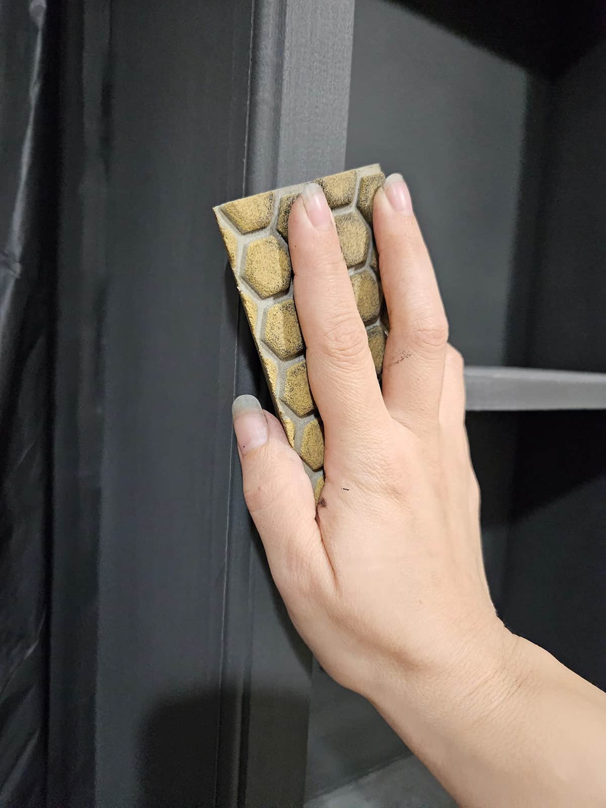 Closeup of a woman's hand sanding black primed cabinets for a smooth finish.