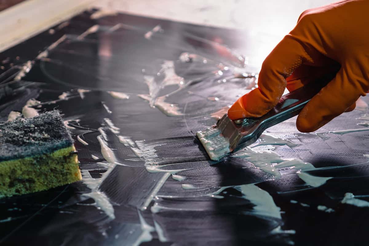 Woman cleaning a glass stove top with a flat razor knife.