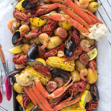 Seafood boil overhead on a table with crab legs, mussels, crawfish, potatoes, corn, and cajun butter sauce.