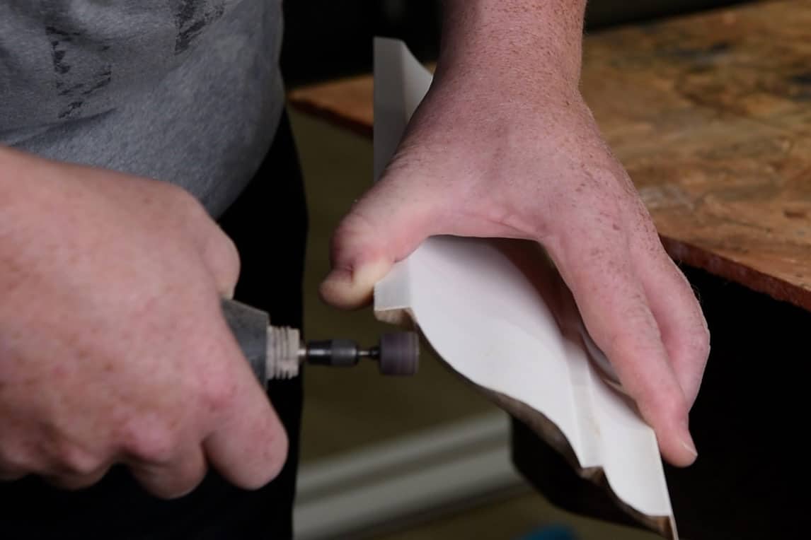 Man using a Dremel sanding drum to shape and adjust a piece of coped molding.