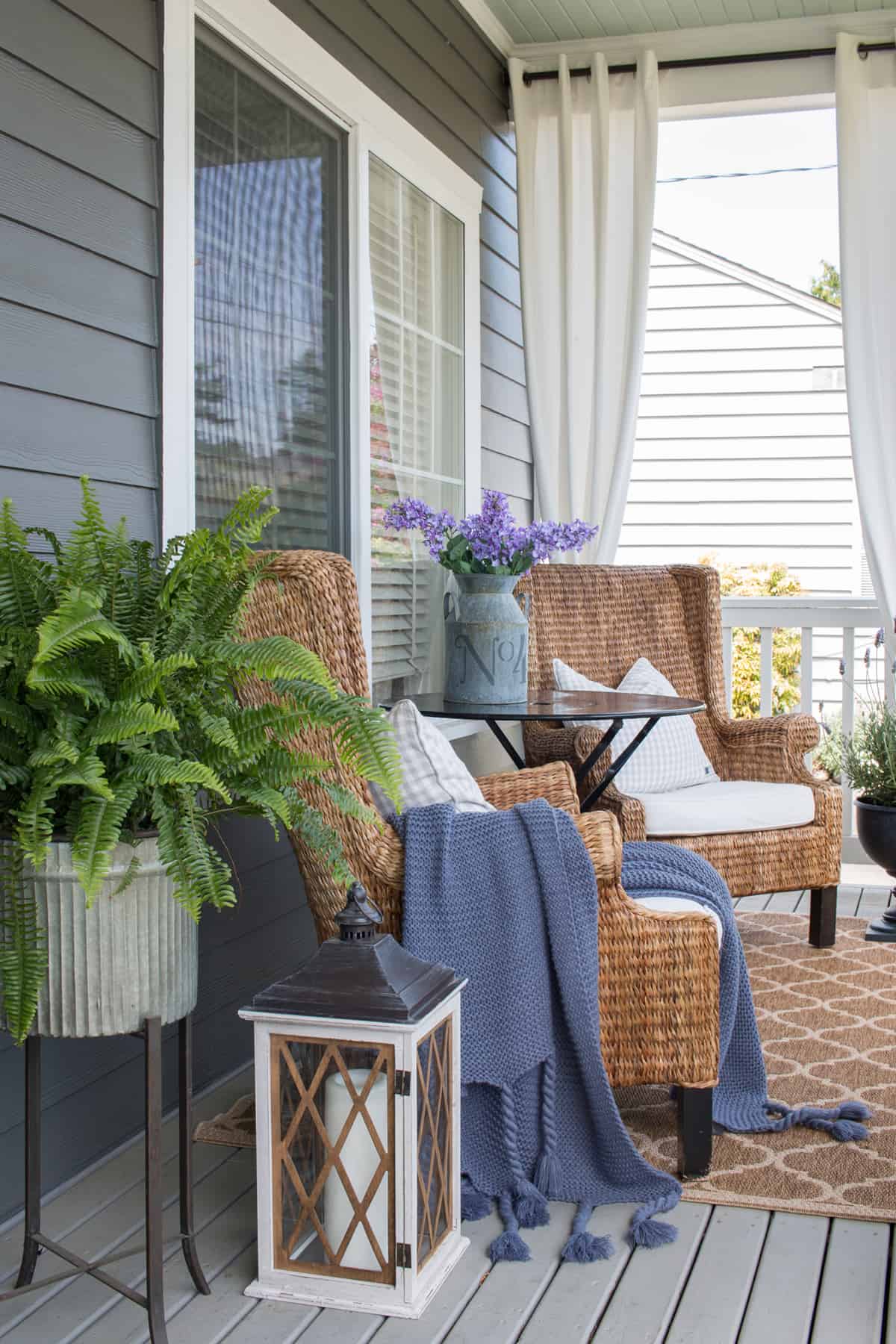 Curtains hung on front porch decorated for spring with cozy rattan and blue & white accessories