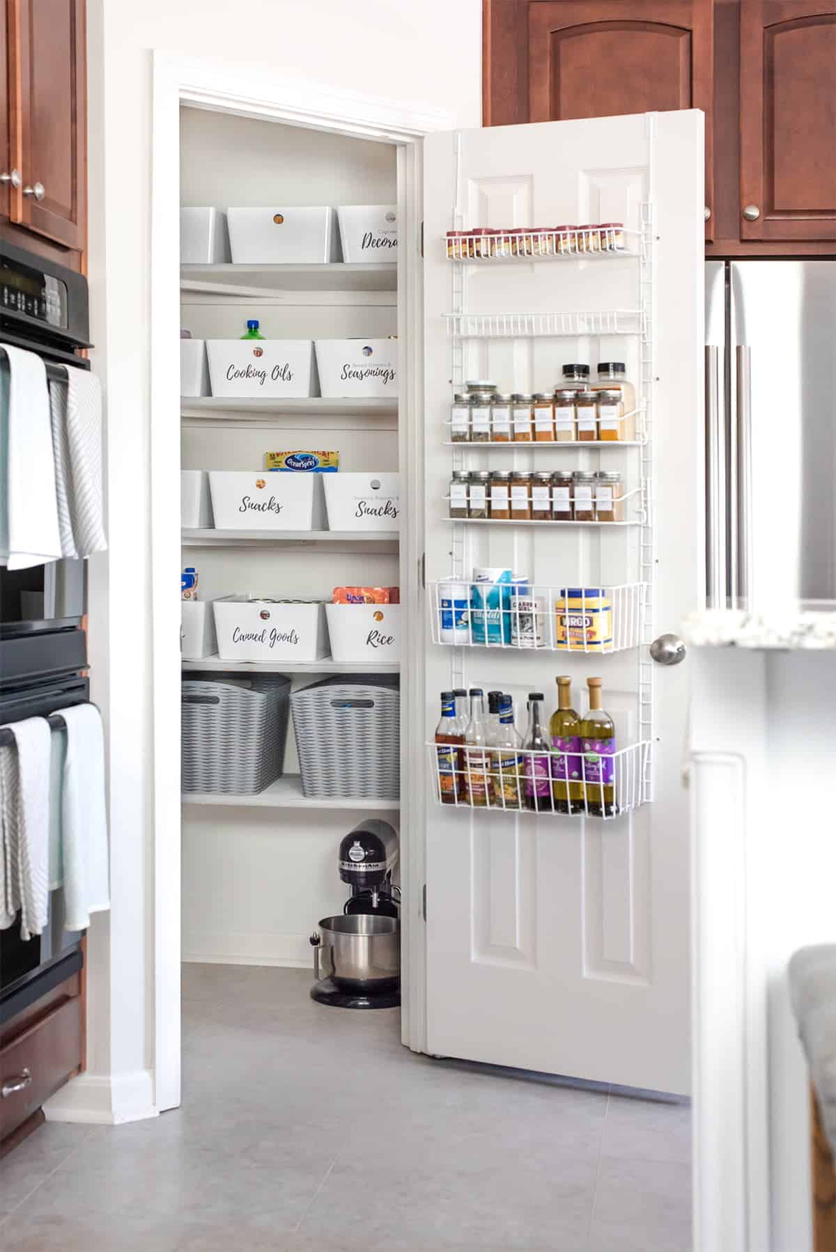 Organized kitchen pantry. Over-the-door storage for spices, labeled uniform bins on shelves.