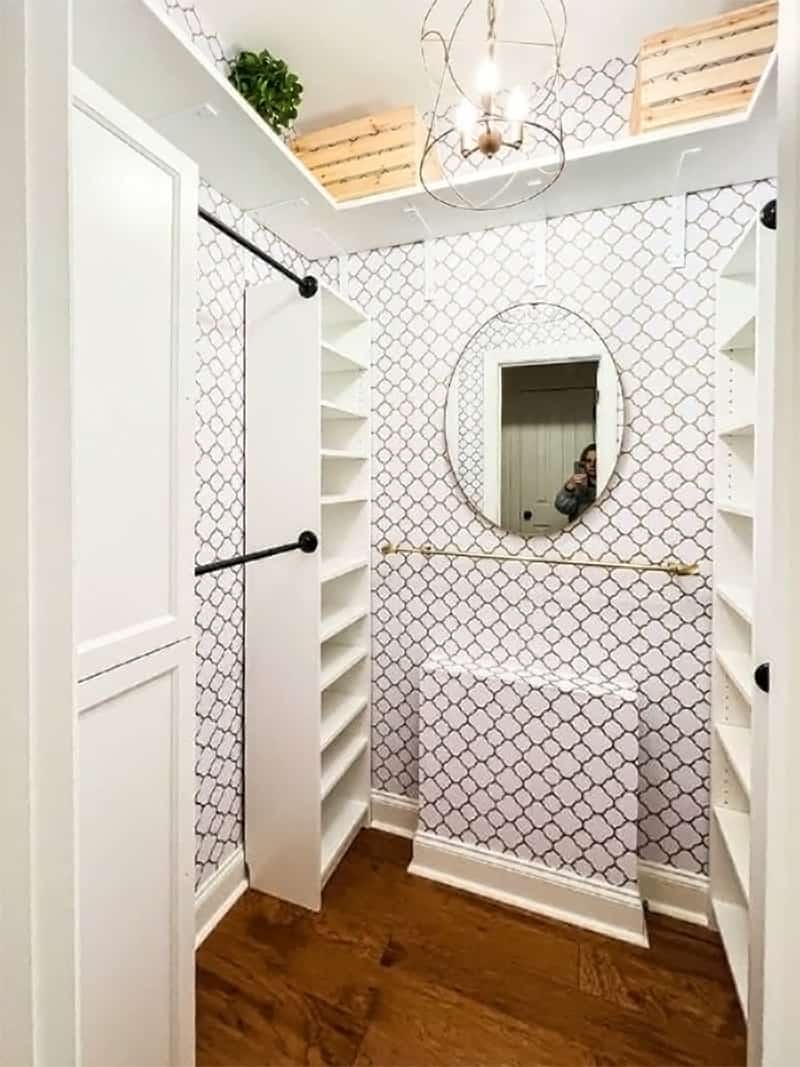 An empty custom closet with lots of shelves and black hanging rods in front of a mirror and wallpaper.