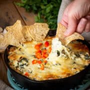 Cheese pull of spinach artichoke dip with hand dipping a tortilla chip.