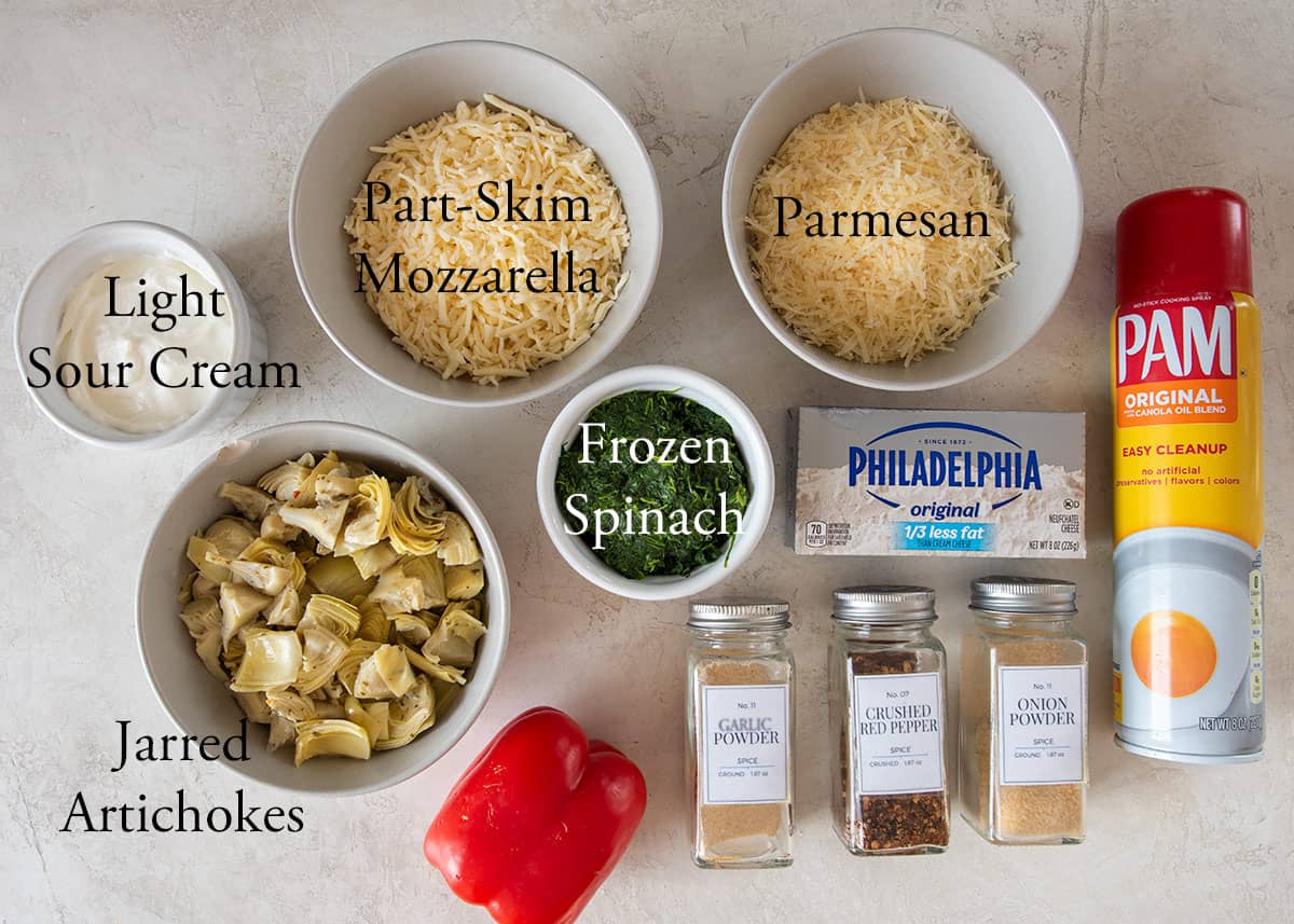 Ingredients to make hot spinach artichoke dip including cheeses, spices, and cream cheese.