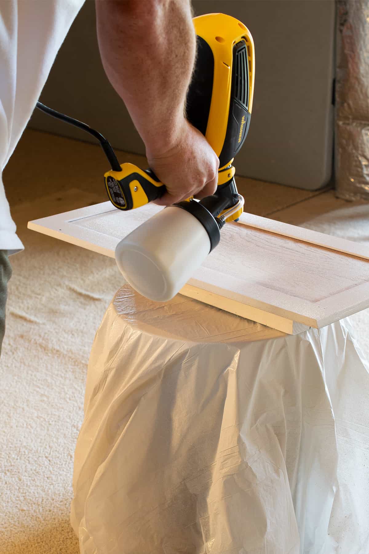 Man spray painting a kitchen cabinet door white.