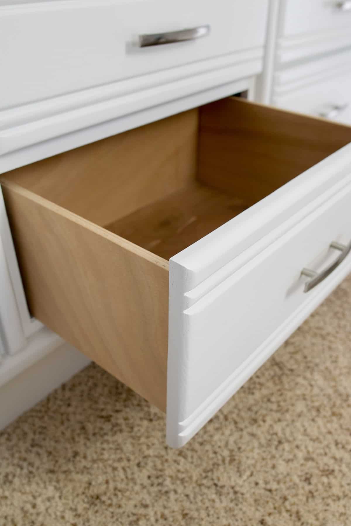 Open drawer on painted white bed with drawer open to show the inside.