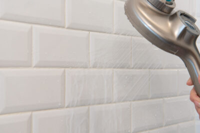 Spraying water on a shower wall with a shower head.