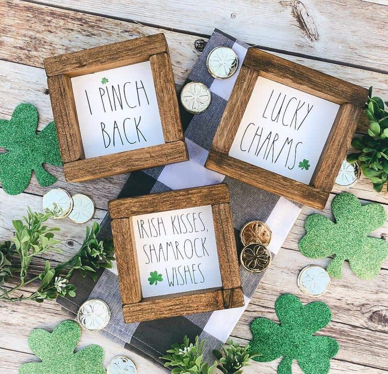 Wood framed St. Patrick's day art on black and white buffalo plaid towel with coins and sparkly shamrock cutouts on wooden planks.