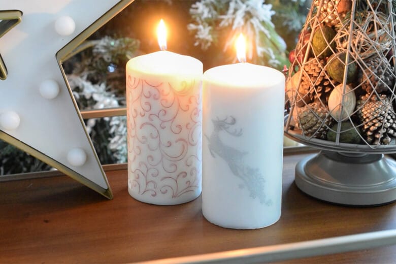 Two lit candles with stamped Christmas designs.