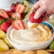 Woman dipping a strawberry into cheesecake dip with graham crackers on top.