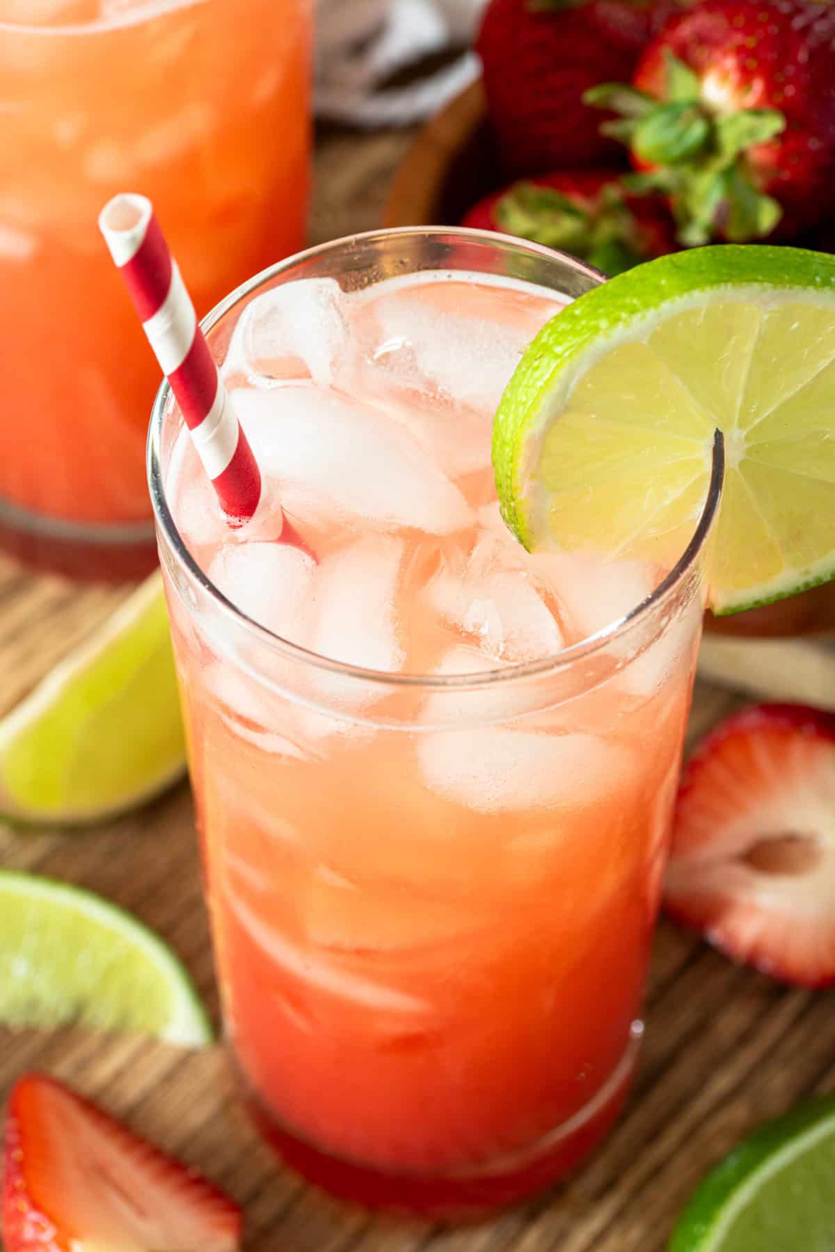 A glass of strawberry limeade with ice and a lime garnish.