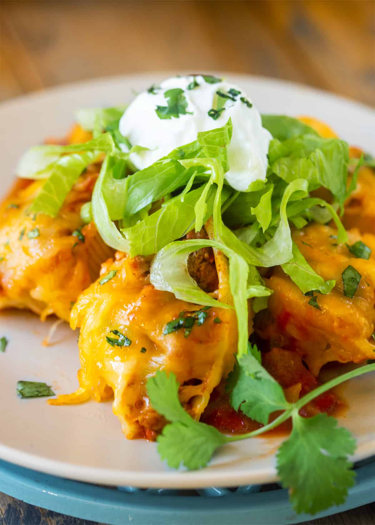 A plate of taco stuffed shells with lettuce and sour cream on top.