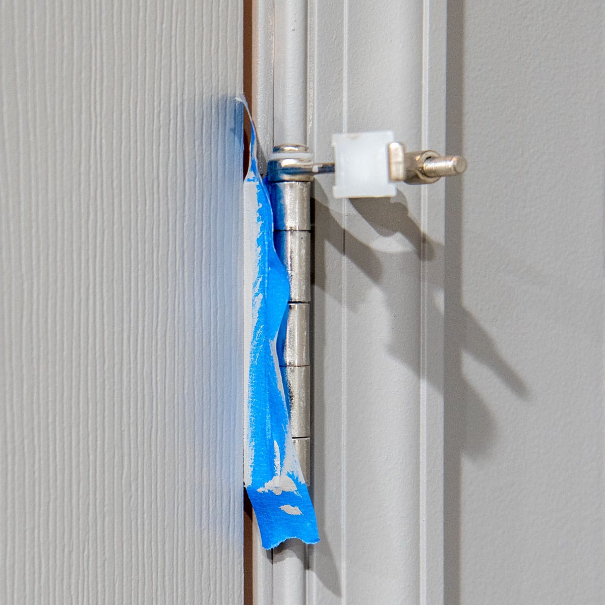 A door hinge shown with painter's tape to keep the paint from splashing on the metal.