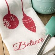 Christmas Stenciled Tea Towels laid on a table jumping reindeer, ornaments, Christmas Tree silhouettes, and text.