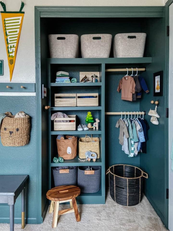 An organized dark cyan closet for baby clothes, laundry hamper, and changing table.