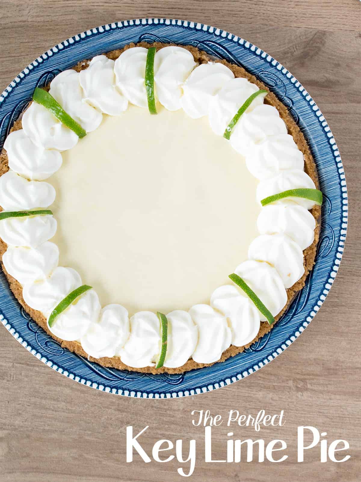 Whole pie viewed top down in blue dish with fresh whipped cream and lime slices.