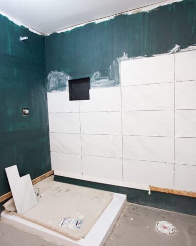 The process of tiling large tiles on a shower wall after waterproofing.