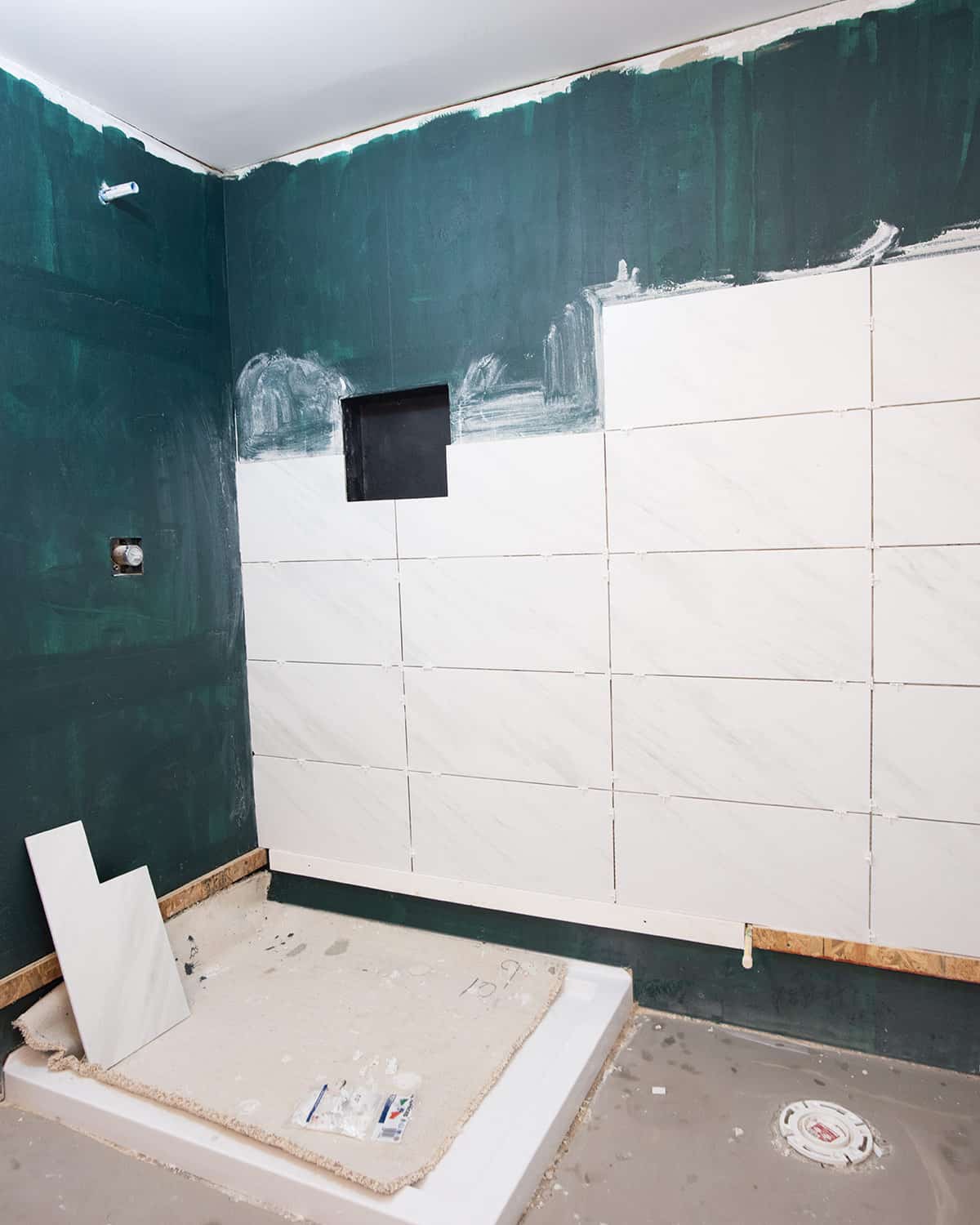 The process of tiling large tiles on a shower wall after waterproofing.