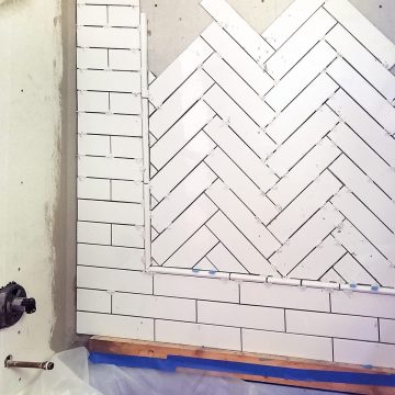 In progress photo of laying herringbone pattern with ceramic tile inset with subway tile surround.
