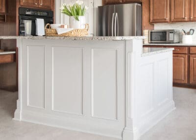 Large grey kitchen island with breakfast bar in traditional trim and two tone different color from the cabinets.