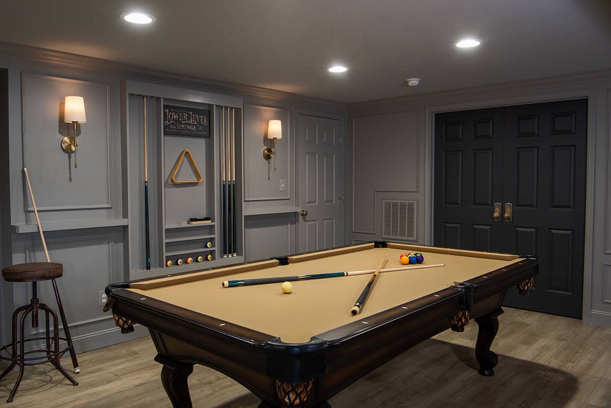 Moody pub basement gray walls with black door and pool table in center.