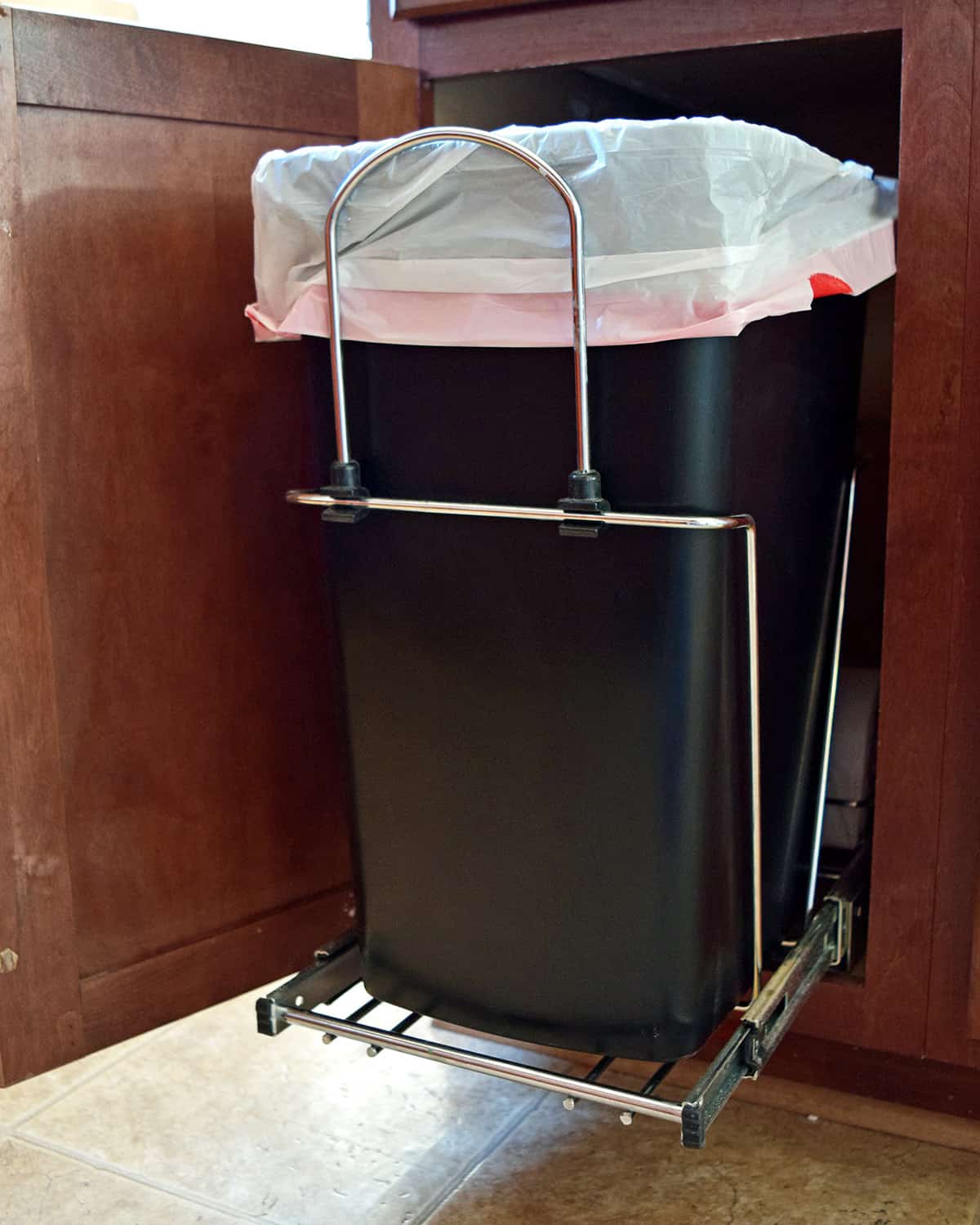A trashcan inside of a cabinet on a pull out roller system.