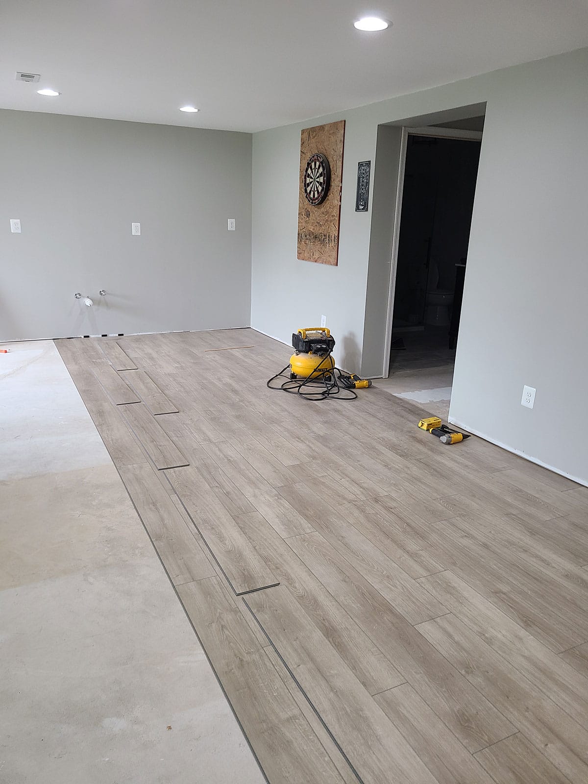 Large room with grey walls in the process of installing rigid wood look vinyl flooring over concrete slab subfloors.