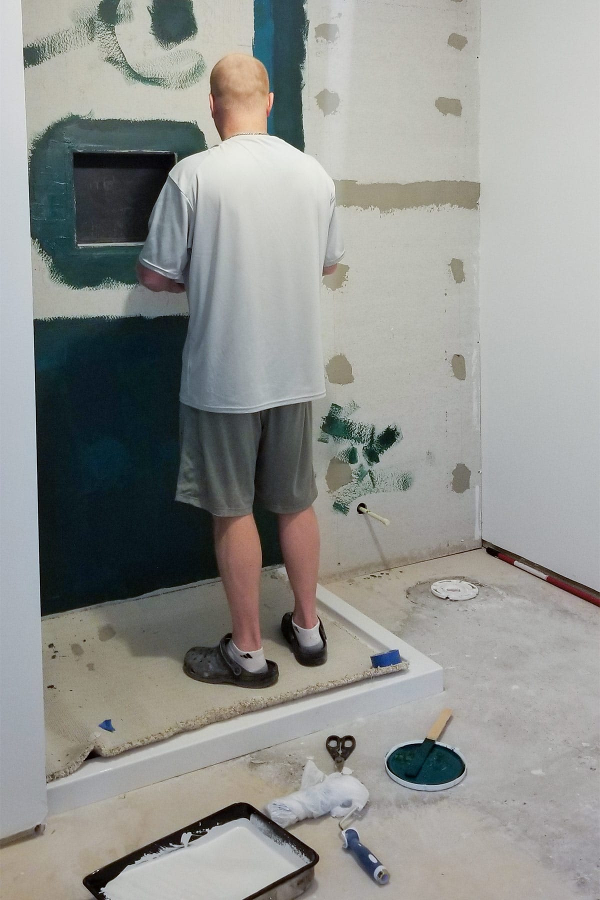 A man painting a liquid waterproofing membrane onto concrete backerboard for a shower installation.