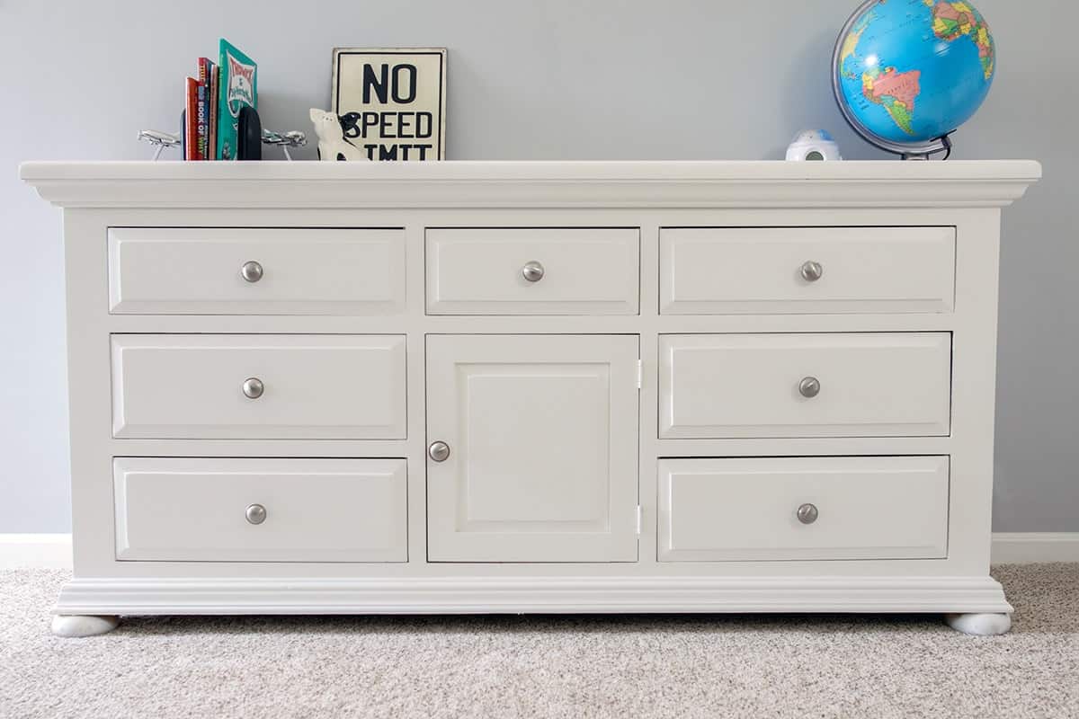 White refinished pine dresser with with satin nickel drawer pulls with nooks and globe on top.